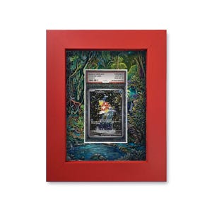 Op de afbeelding: Een rood omlijst kunstwerk met een beoordeelde ruilkaart met een kleurrijke illustratie van een personage voor een waterval. De achtergrond is een gedetailleerde junglescène met een vijver.