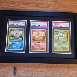 May include: Three Pokemon trading cards, Squirtle, Charmander, and Bulbasaur, are displayed in a black frame. The cards are from the 1999 Pokemon Game series and are in mint condition.