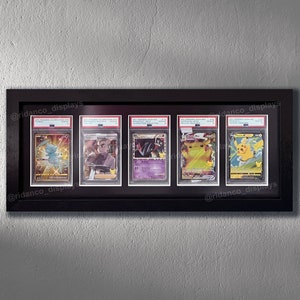 Op de afbeelding: Vijf Pok&eacute;mon-verzamelkaarten worden tentoongesteld in een zwart frame met een witte passe-partout. De kaarten zijn ingekapseld in beschermende plastic hoesjes. De kaarten tonen Pikachu, Charizard en andere Pok&eacute;mon-personages. Het frame is gelabeld met de social media-handle "@ridanco_displays".