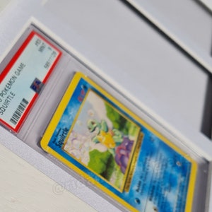 May include: A graded 1999 Pokemon Game Squirtle card in a protective case. The card features a blue background with an illustration of Squirtle, a water-type Pokemon, in a grassy field.