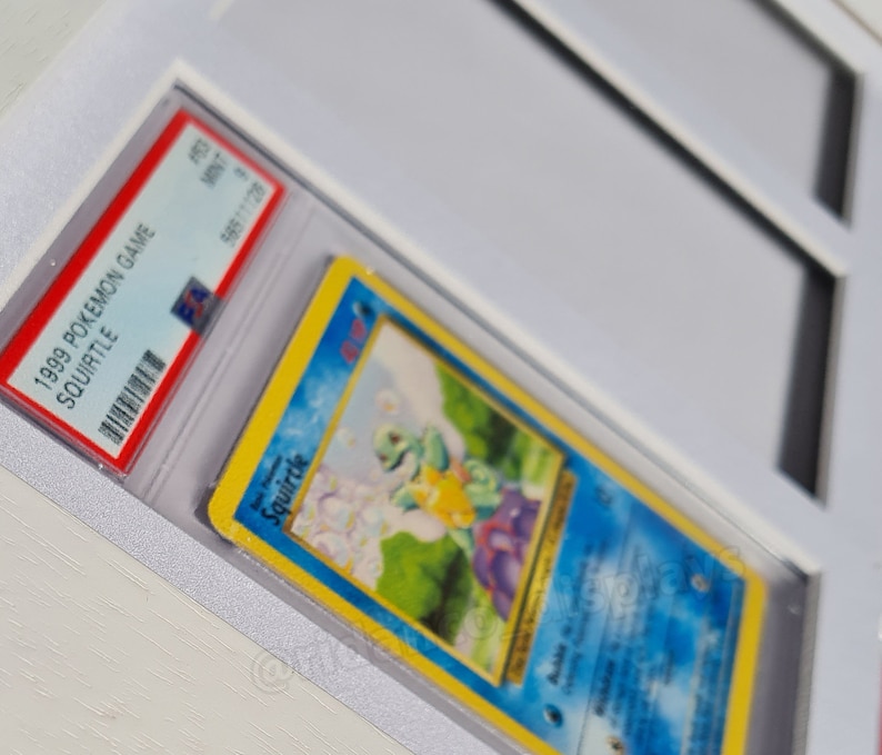May include: A graded 1999 Pokemon Game Squirtle card in a protective case. The card features a blue background with an illustration of Squirtle, a water-type Pokemon, in a grassy field.