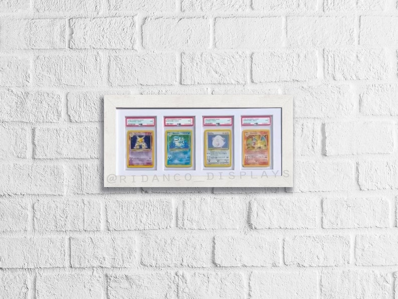 May include: Five Pokemon cards are displayed in a white frame on a white brick wall. The cards are encased in protective plastic sleeves. The cards feature the Pokemon characters Venusaur, Blastoise, Charizard, Jolteon, and Vaporeon. The frame has the text "@ridanco_displays" at the bottom.