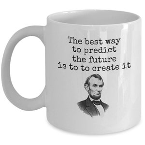 Op de afbeelding: Witte keramische koffiemok met een zwart-witte afbeelding van Abraham Lincoln en de quote "De beste manier om de toekomst te voorspellen is om hem te creëren".