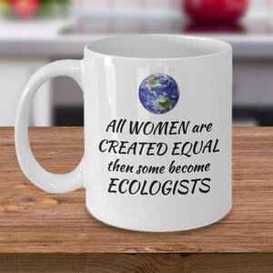 Peut inclure: Une tasse en céramique blanche avec un graphique noir d'un globe terrestre et le texte "All women are created equal then some become ecologists".