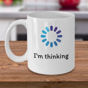 May include: White ceramic coffee mug with a blue and purple loading icon and the text "I'm thinking".