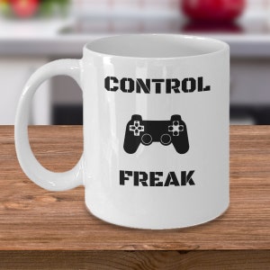 May include: White ceramic mug with a black graphic of a video game controller and the text "CONTROL FREAK".