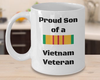 May include: White ceramic coffee mug with black text that reads "Proud Son of a Vietnam Veteran". A green, yellow, and red ribbon is printed below the text.