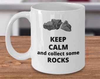 May include: White ceramic mug with a black graphic that says "Keep Calm and collect some ROCKS". Three grey rocks are pictured above the text.