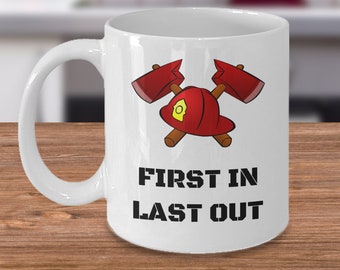 Puede incluir: Taza de café de cerámica blanca con un casco de bombero rojo y hachas cruzadas. El texto "FIRST IN LAST OUT" está impreso en negro debajo del gráfico.