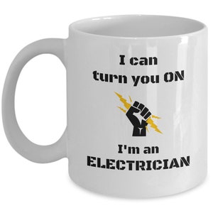 May include: White ceramic coffee mug with a black and yellow graphic. The graphic features a fist with a lightning bolt and the text "I can turn you ON I'm an ELECTRICIAN".