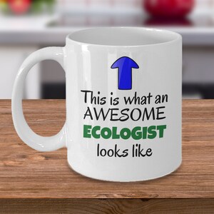 Peut inclure: Une tasse à café en céramique blanche avec une flèche bleue pointant vers le haut et le texte "This is what an AWESOME ECOLOGIST looks like".
