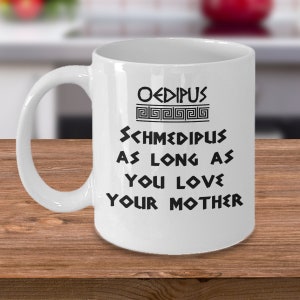 May include: White ceramic coffee mug with black text that reads "Oedipus Schmedipus As Long As You Love Your Mother". The text is in a stylised font with a Greek key design above the word "Oedipus".