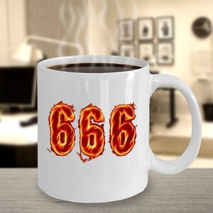 May include: White ceramic coffee mug with a black handle. The mug has a graphic of the number 666 in flames.
