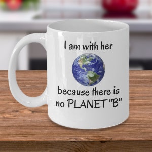Può includere: Tazza in ceramica bianca con una grafica nera che recita "I am with her because there is no PLANET "B"". La grafica include anche un'immagine blu e verde della Terra.
