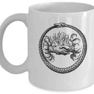 May include: White ceramic coffee mug with a black and white illustration of a snake biting its own tail, forming a circle. Inside the circle, two hands are shaking, surrounded by clouds and flames.
