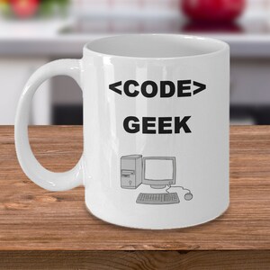 Puede incluir: Taza de café de cerámica blanca con un diseño negro que dice "<CODE> GEEK" y una ilustración en blanco y negro de una computadora.