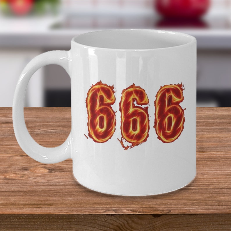 May include: White ceramic coffee mug with a design of the number 666 in flames.