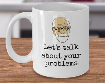 Puede incluir: Taza de café de cerámica blanca con una ilustración en blanco y negro de Sigmund Freud. La taza tiene el texto "Let's talk about your problems" impreso en ella.