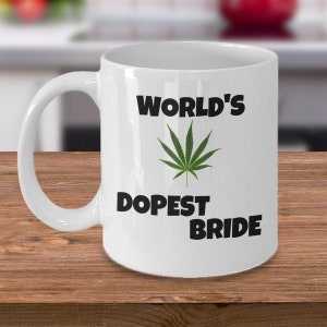 May include: White ceramic mug with black text that reads "World's Dopest Bride" and a green marijuana leaf graphic.