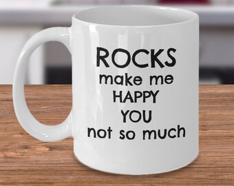 May include: White ceramic coffee mug with black text that reads "Rocks make me happy you not so much".