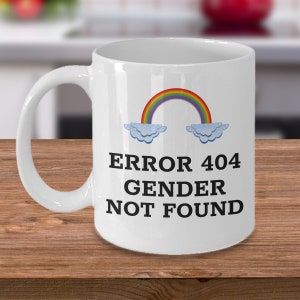 May include: White ceramic coffee mug with a rainbow, clouds, and the text "ERROR 404 GENDER NOT FOUND".