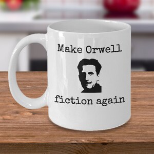 Puede incluir: Taza de café de cerámica blanca con una silueta negra de George Orwell y el texto "Make Orwell fiction again".