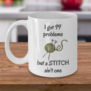 May include: White ceramic mug with a green yarn ball and knitting needles, and the text "I got 99 problems but a STITCH ain't one".