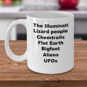 May include: White ceramic coffee mug with black text that reads "The Illuminati Lizard people Chemtrails Flat Earth Bigfoot Aliens UFOs"