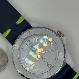 May include: A gray watch with a black leather band and a green stitching. The watch face has a white background with black numbers and a colorful design.