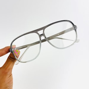 Puede incluir: Gafas de estilo aviador grises con lentes transparentes. La montura es de plástico translúcido.