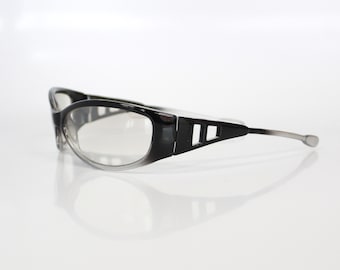 May include: Black and gray eyeglasses with clear lenses. The frames are a glossy black with a gray gradient towards the lenses. The temples are a thin, silver color, and the design includes three rectangular cutouts on the sides.
