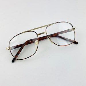 May include: Gold-rimmed glasses with tortoise shell frames. The glasses have clear lenses.