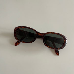 May include: Tortoiseshell oval sunglasses with dark lenses.