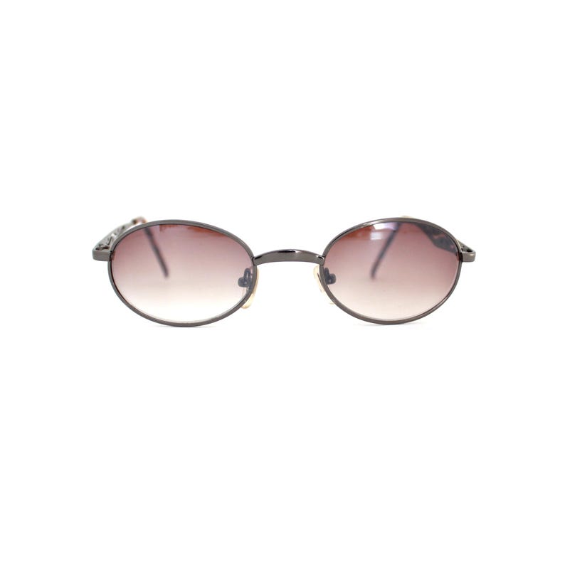 Pode incluir: Um par de &oacute;culos de sol ovais com lentes de degrad&ecirc; marrom escuro e arma&ccedil;&atilde;o de metal prateado.