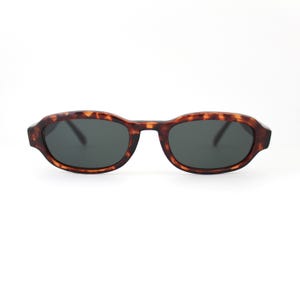 May include: Tortoise shell oval sunglasses with dark gray lenses.