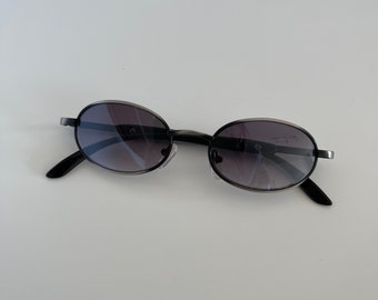 May include: A pair of oval-shaped sunglasses with black frames and dark gray lenses.