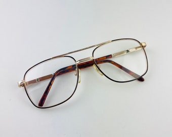 Puede incluir: Gafas de montura dorada con patillas de carey marrón. Las lentes son transparentes.