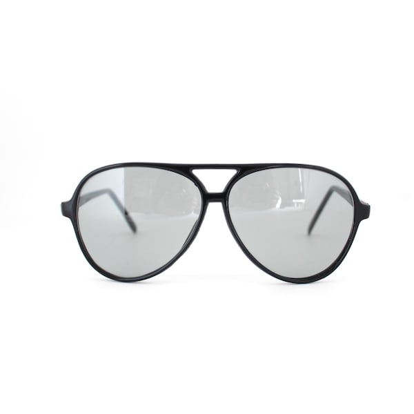 May include: Black aviator sunglasses with grey lenses. The sunglasses have a classic teardrop shape and a black frame. The lenses are reflective, and the sunglasses are set against a white background.