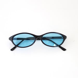 May include: Black oval-shaped sunglasses with blue lenses. The sunglasses have a polished black frame and the text "POLISHED FRAMES" is printed on the right side of the frame.