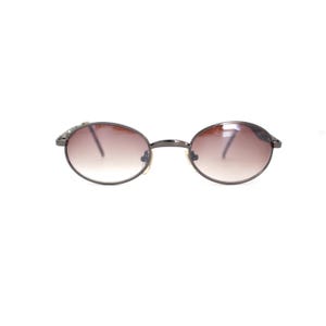 Pode incluir: Um par de &oacute;culos de sol ovais com lentes de degrad&ecirc; marrom e arma&ccedil;&atilde;o de metal prateado.