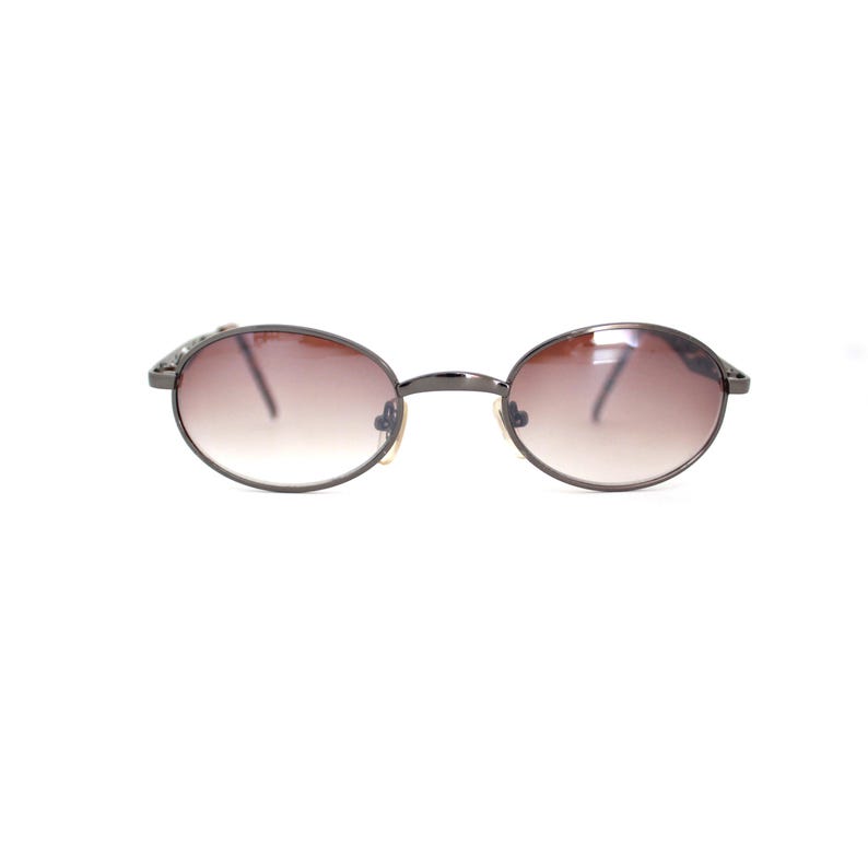 Pode incluir: Um par de &oacute;culos de sol ovais com lentes de degrad&ecirc; marrom e arma&ccedil;&atilde;o de metal prateado.