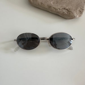 May include: Silver oval-shaped sunglasses with dark grey lenses.