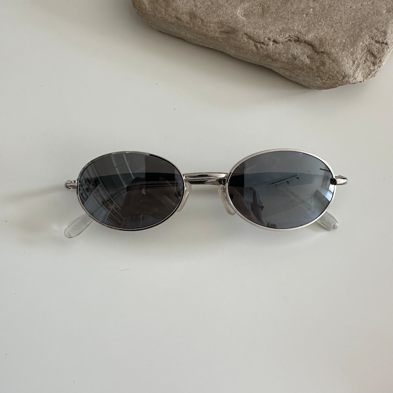 May include: Silver oval-shaped sunglasses with dark grey lenses.