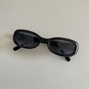 Peut inclure: Lunettes de soleil ovales noires avec des verres foncés.