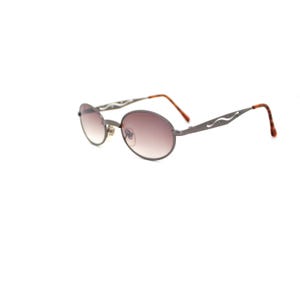 Pode incluir: Um par de &oacute;culos de sol ovais com arma&ccedil;&atilde;o de metal prateado e lentes marrons. A arma&ccedil;&atilde;o tem um design decorativo com uma linha ondulada de cada lado.