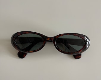 May include: Tortoise shell oval sunglasses with dark lenses.
