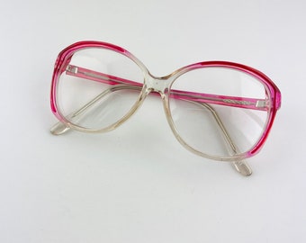 May include: Clear plastic eyeglasses with a pink frame. The frame is thick and has a rounded shape.