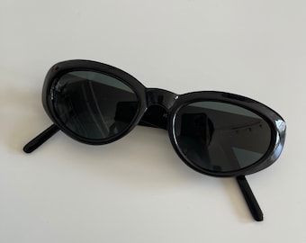 Puede incluir: Gafas de sol ovaladas negras con lentes oscuros.