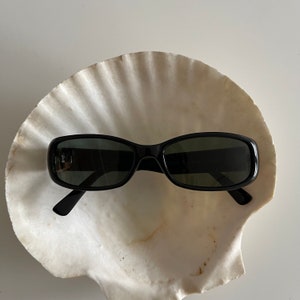 May include: Black rectangular sunglasses with dark lenses, resting on a white seashell.