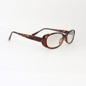 May include: Tortoiseshell oval-shaped eyeglasses with clear lenses.